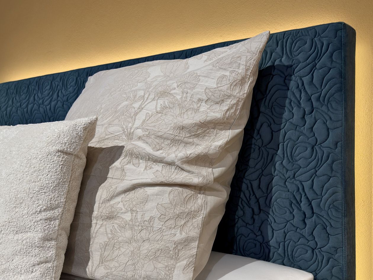 Kissen vor dem blauen Kopfteil des Betts im Musterzimmer